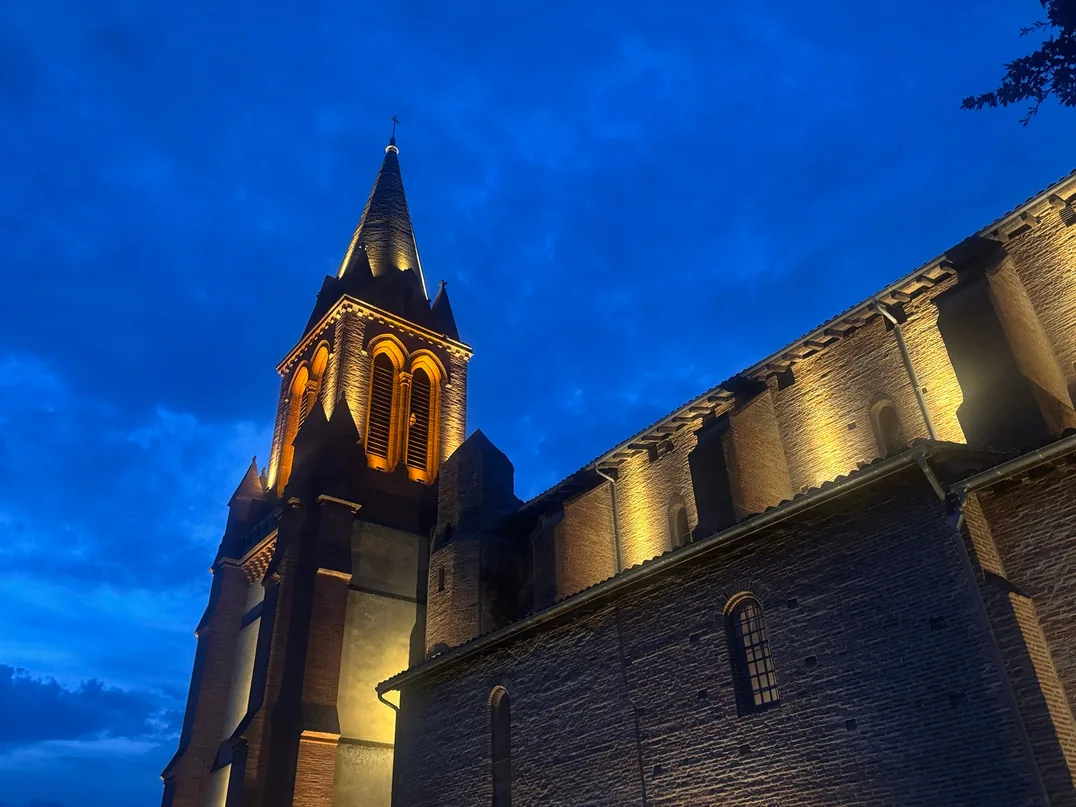 Église de Castelnau-d'Estrétefonds illuminée de nuit, clocher et façade en briques — mise en lumière LED par MIDI LUM